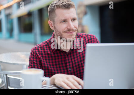 Giovane uomo a Outdoor Cafe lavorando sul computer portatile Foto Stock