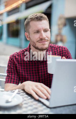 Giovane uomo a Outdoor Cafe lavorando sul computer portatile Foto Stock