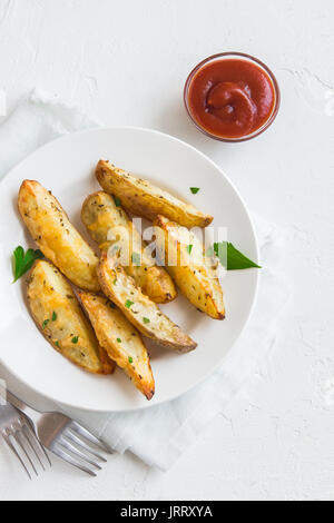 Patate al forno cunei con formaggio ed erbe e salsa di pomodoro sulla piastra bianca - Casalinghi vegetale organico vegetariano vegano Spicchi di patate snack alimentare Foto Stock