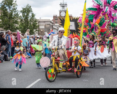 Didascalia 62/150 persone a cavallo dei tricicli e marciando verso il basso la High Street in abiti colorati a Stockton International Riverside Festival parade Foto Stock