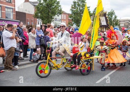 Didascalia 62/150 persone a cavallo dei tricicli e marciando verso il basso la High Street in abiti colorati a Stockton International Riverside Festival parade Foto Stock