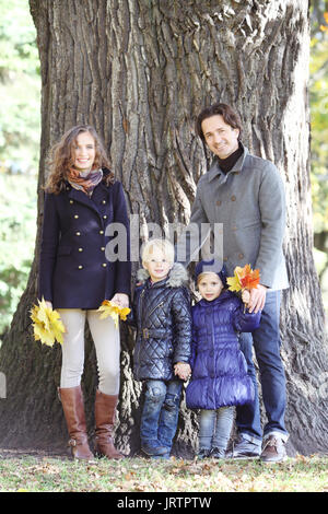 La famiglia felice in autunno park vicino al grande tronco di albero Foto Stock