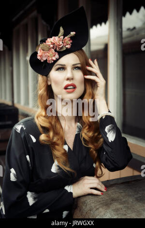 Giovane donna in abiti d'epoca e floreale hat appoggiato su di valigie su Severn Valley Railway Station platform Foto Stock