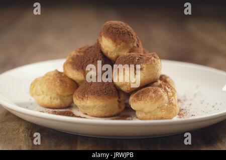 Profiteroles ricoperti di polvere di cacao su piastra bianca sul tavolo di legno Foto Stock