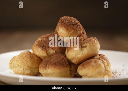 Closeup colpo di profiteroles ricoperti di polvere di cacao su piastra bianca sul tavolo di legno Foto Stock