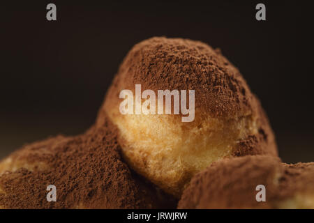 Closeup colpo di profiteroles ricoperti di polvere di cacao su piastra bianca sul tavolo di legno Foto Stock