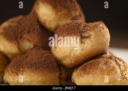 Closeup colpo di profiteroles ricoperti di polvere di cacao su piastra bianca sul tavolo di legno Foto Stock