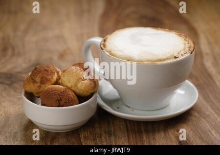 Cappuccino con profiteroles sulla tavola di legno Foto Stock