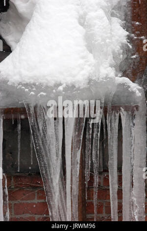 Neve spessa e ghiaccioli sospesi dal tetto di un edificio di mattoni rossi Foto Stock