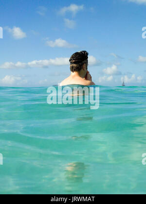 Uomo caucasico con snorkeling maschera in piedi in tropical acque turchesi e guardando una barca a vela a distanza Foto Stock