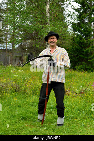 Di mezza età contadino nel vecchio abbigliamento vintage mows erba sul prato tradizionale falce in legno Foto Stock