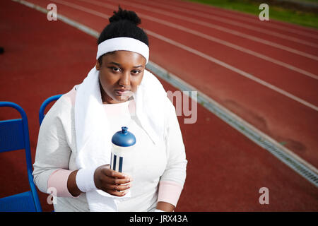 Donna afro-americana in appoggio e acqua potabile dopo il jogging sulla via Foto Stock