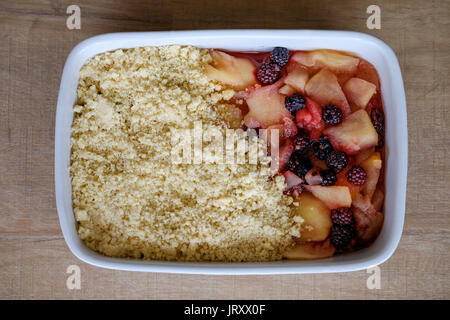 Un tradizionale crumble inglese parzialmente fatto di mele e mora. La torta è in una grande teglia in ceramica e pronta per essere cotta Foto Stock