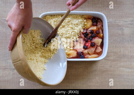 Un cuoco prepara e aggiunge il crumble mix di un tradizionale inglese e apple budino di blackberry Foto Stock