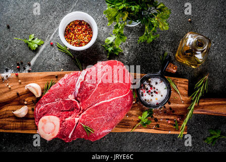 Carne cruda con gli ingredienti per cucinare. Filetto di manzo, filetto sul tessuto osseo, su di un tagliere con sale, pepe, prezzemolo e rosmarino, olio d'oliva, aglio, s Foto Stock