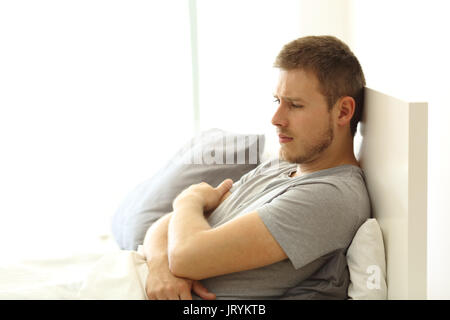 Triste singolo uomo che guarda lontano sul letto di una camera di hotel o appartamento Foto Stock