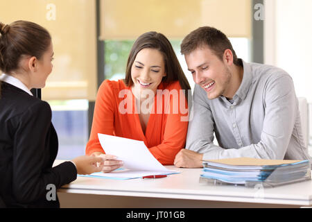 Commessa a parlare con un paio di clienti soddisfatti in seduta un desktop in ufficio Foto Stock