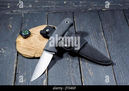 Il cacciatore di coltello con fodero e bussola su un nero lo sfondo di legno. Foto Stock