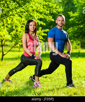 L uomo e la donna a fare esercizi di stretching al summer park. Coppia giovane esercizio e stretching i muscoli prima della attività sportiva - outdoor in natura Foto Stock