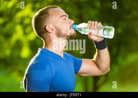 Sport atletici uomo acqua potabile da una bottiglia. Bevanda fredda dopo fitness all'aperto. Foto Stock