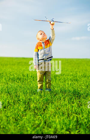 Felice ragazzo giocando con aeroplano giocattolo contro il Cielo di estate blu e verde dello sfondo dei campi. Foto Stock