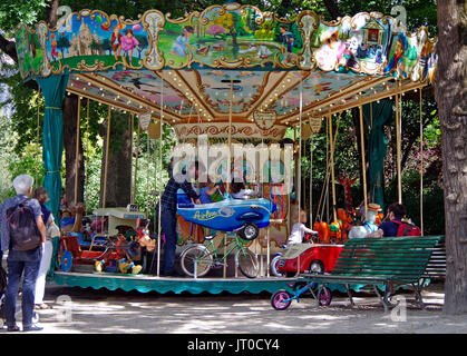 Bambini che viaggiano su una piccola giostra, Square des Batignolles Parigi Francia, mentre i genitori e i nonni troppo, ammirare e fotografare. Foto Stock