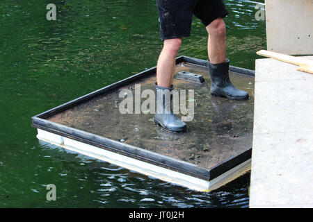 Square zattera per ponte opere di riparazione galleggia sull'acqua. Il lavoratore è su una zattera e vincola una cassaforma di legno per la ringhiera per decorare la vacanza. Foto Stock