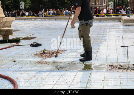 Londra REGNO UNITO. Il 7 agosto 2017. Un lavoratore del consiglio spazza e raccoglie le monete gettate dai membri del pubblico mentre si pulisce le fontane in Trafalgar Square Foto Stock