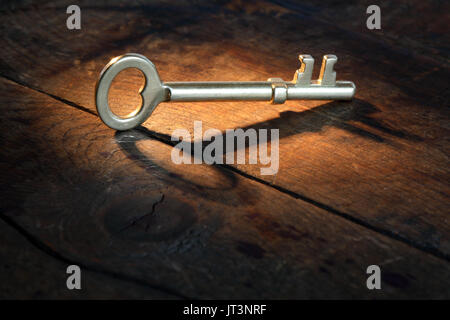 Primo piano di vintage golden key permanente sulla vecchia superficie di legno con il fascio di luce Foto Stock