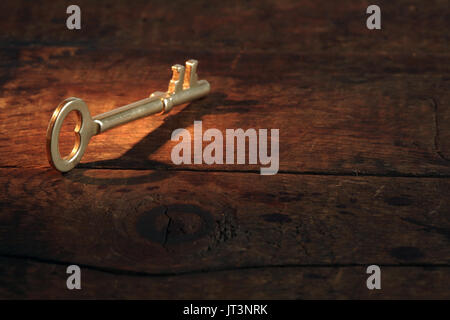 Primo piano di vintage golden key permanente sulla vecchia superficie di legno con il fascio di luce Foto Stock