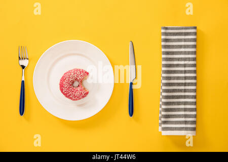 Vista aerea del morso ciambella con smalto rosa nella piastra e igienico isolati su giallo. sfondo in stile minimalista Foto Stock