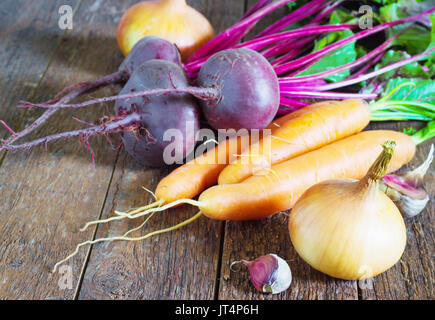 Diversi giovani freschi ortaggi barbabietole carote, pomodori, aglio, cipolle giacciono su di un tavolo di legno. Stile rustico Foto Stock