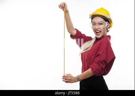 Donna asiatica engineer indossare l'elmetto di sicurezza e occhiali di sicurezza giocando con il nastro di misurazione nelle sue mani. ingegneria industriale e concetto di occupazione Foto Stock