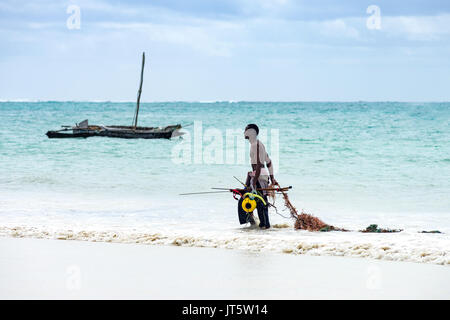 Pescatore tira net lungo il litorale dopo il ritorno dalla pesca con la tradizionale barca dhow in background, Diani, Kenya Foto Stock