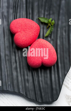 Close-up di decorate splendidamente delizioso rosso a forma di cuore strowberry dessert su una pietra nera piastra. Foto Stock