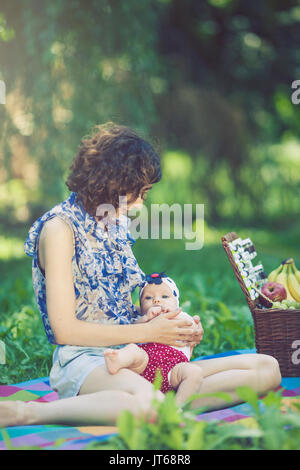 Giovane bella madre siede su una coperta con sua figlia durante un picnic nel parco Foto Stock