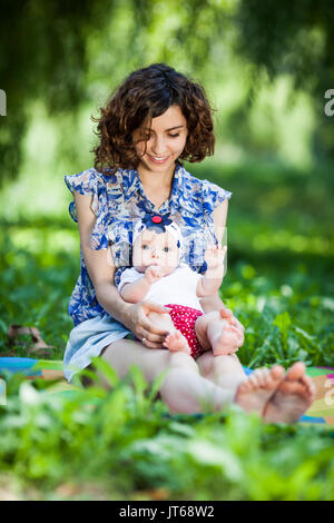 Giovane bella madre siede su una coperta con sua figlia durante un picnic nel parco Foto Stock