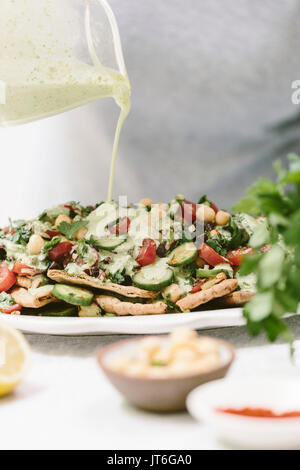 Pane Pita condito con insalata greca e tahini medicazione è fotografato come una donna è drizzling con il tahin medicazione. Foto Stock