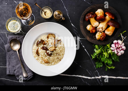 Risotto con funghi porcini su piastra e materie di funghi in marmo scuro dello sfondo della tabella Foto Stock