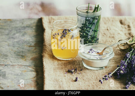 Materie organiche di miele, zucchero bianco in vasetti di vetro, vetro di acqua aromatizzata con fiori di lavanda, in piedi sul tavolo con il sacco. In stile rustico, la luce del giorno. Foto Stock