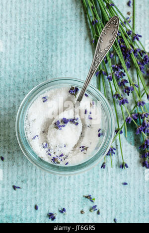 Zucchero bianco in vasetti di vetro aromatizzato con fiori di lavanda con cucchiaino su turchese sfondo texture. Vista dall'alto. In stile rustico, la luce del giorno. Foto Stock