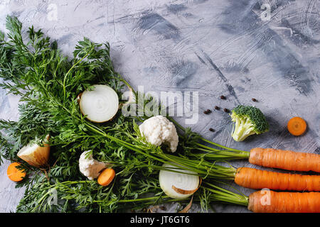 Verdure crude per la cottura della zuppa. Ingredienti giovani carota con haulm, broccoli, cavolfiori, cipolla, aglio, sale pepe su cemento grigio Sfondo. Foto Stock