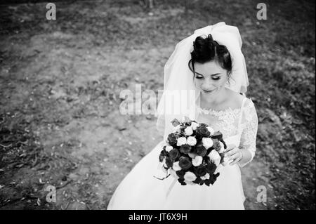 Ritratto di una fantastica sposa indossando splendidi abiti da sposa e velo pone con un bouquet. Foto in bianco e nero. Foto Stock