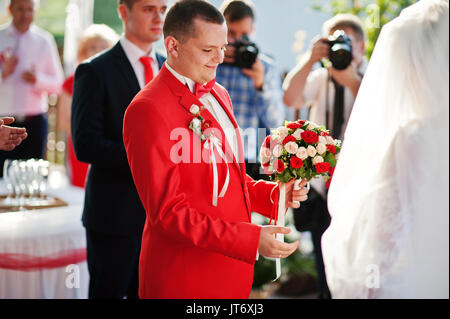 Ritratto di un bel lo sposo in smoking rosso azienda wedding bouqet all'aperto. Foto Stock