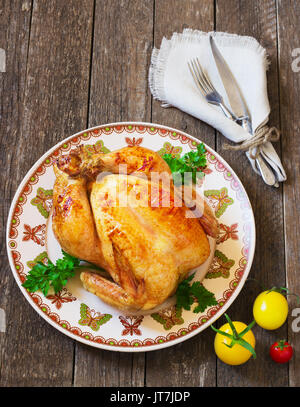 Tutto il pollo arrosto con pomodori e posate su un tavolo di legno Foto Stock