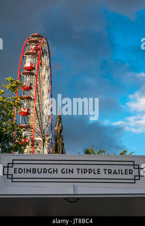 Edimburgo, Scozia, Regno Unito, 7 agosto 2017. Vista la festa grande ruota e la parte superiore del monumento di Scott, Princes Street, Edinburgh, con segnaletica di primo piano di un festival all'aperto uscita Gin Foto Stock