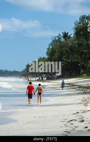 Un giovane a piedi lungo il tropical spiaggia di sabbia bianca litorale in una giornata di sole, Diani, Kenya Foto Stock