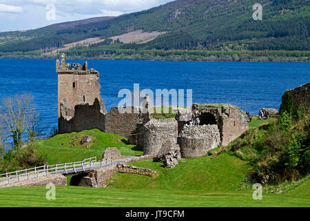 Rovine di storico castello Urquart accanto all acqua blu di Loch Ness con colline boscose in background vicino a Inverness, Scotland Foto Stock