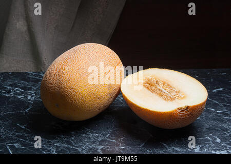 Tutto mature e metà di melone Honeydew frutta nel periodo estivo sul marmo scuro dello sfondo. Foto Stock