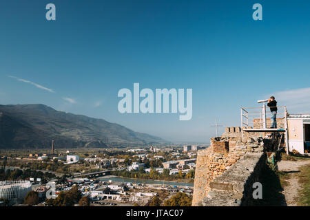 Gori, Shida Kartli Regione, Georgia. Uomo cerca turistica attraverso un gettone binocolo sul paesaggio urbano di pareti di Gori fortezza nel giorno di sole. Goris Foto Stock